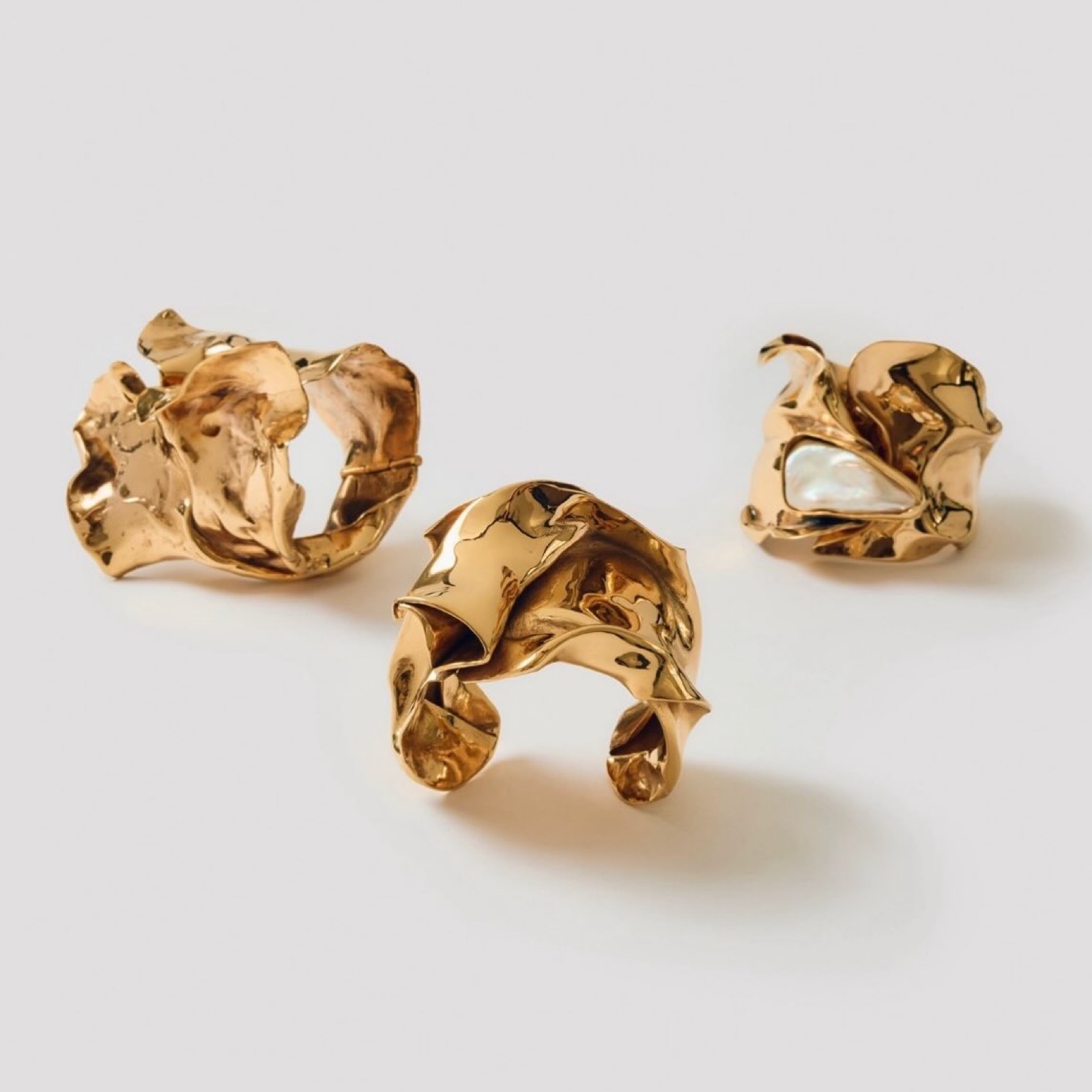 Three Crushed Cuffs in polished bronze on a cream ground
